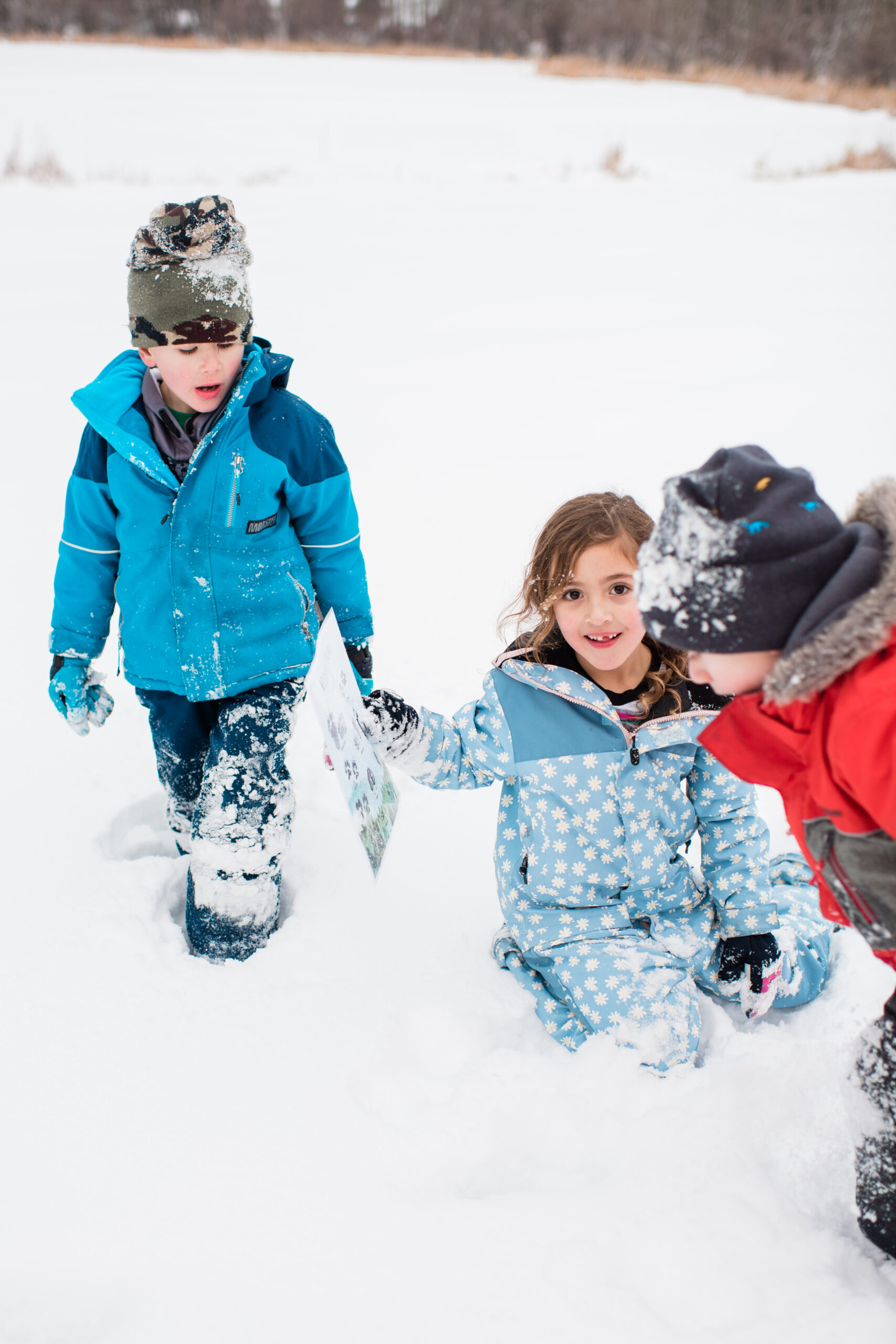 three kids in snow gear looking at an animal footprint in the snow