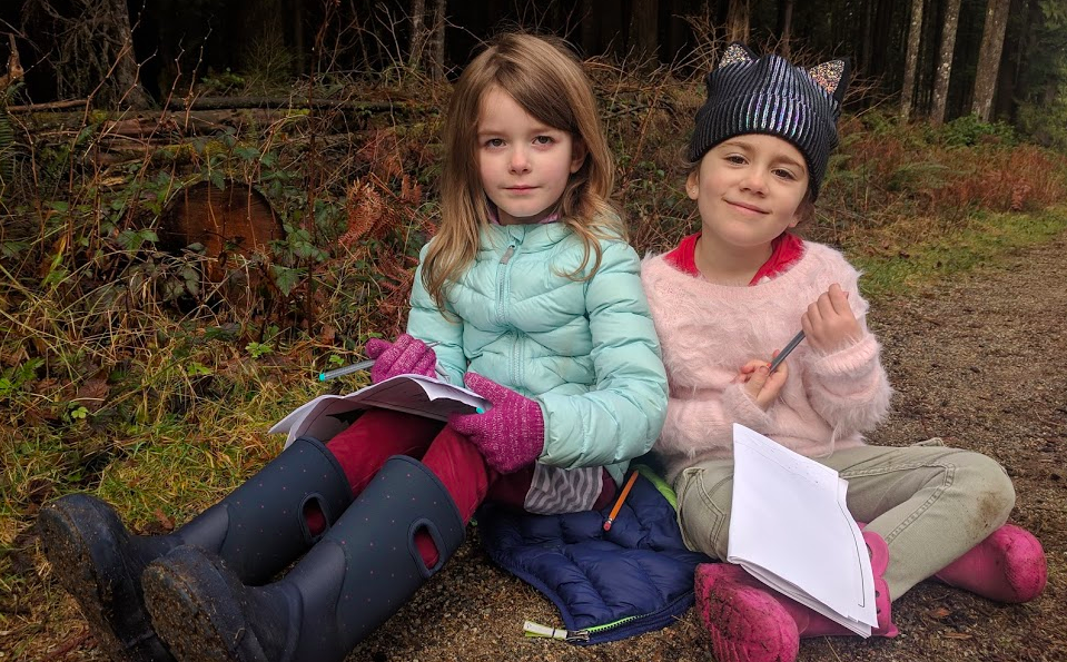 Two girls sitting in the forest writing in their workbooks at Wild & Immersive Spring Break Camp