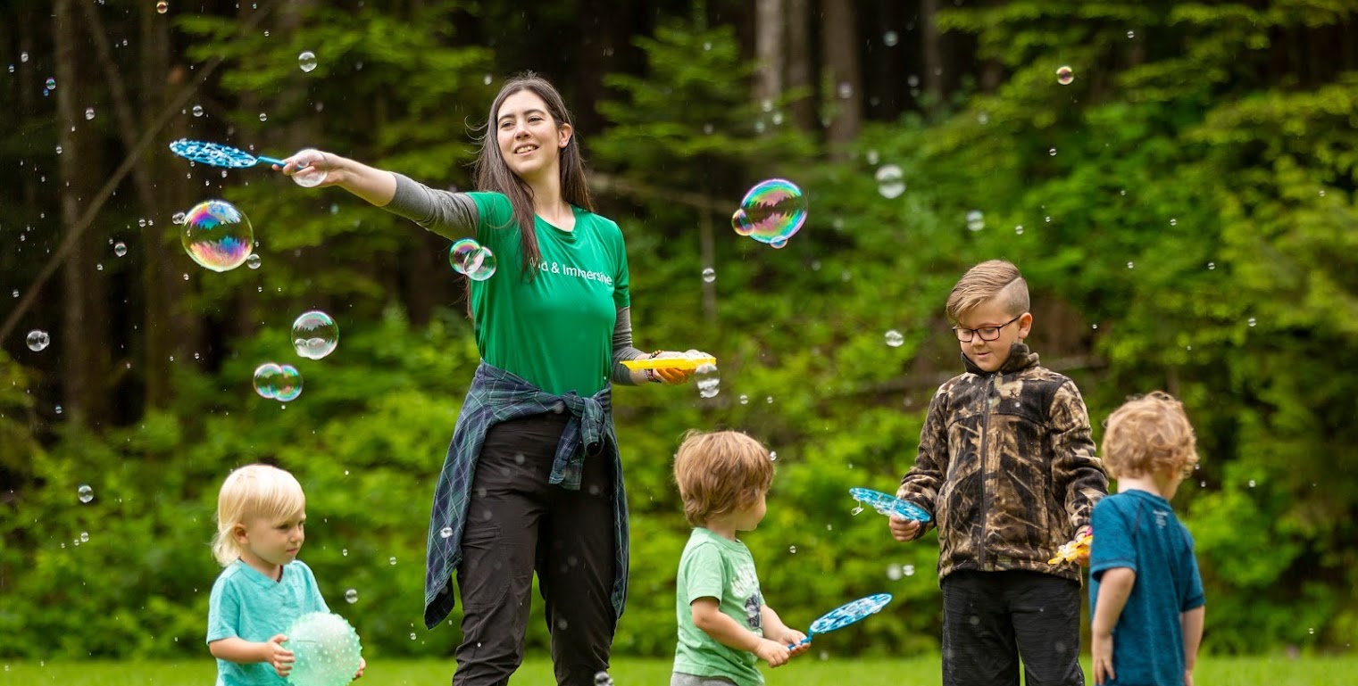A group of kids with a leader blowing bubbles in a field at one of wild and immersive's spring break camps
