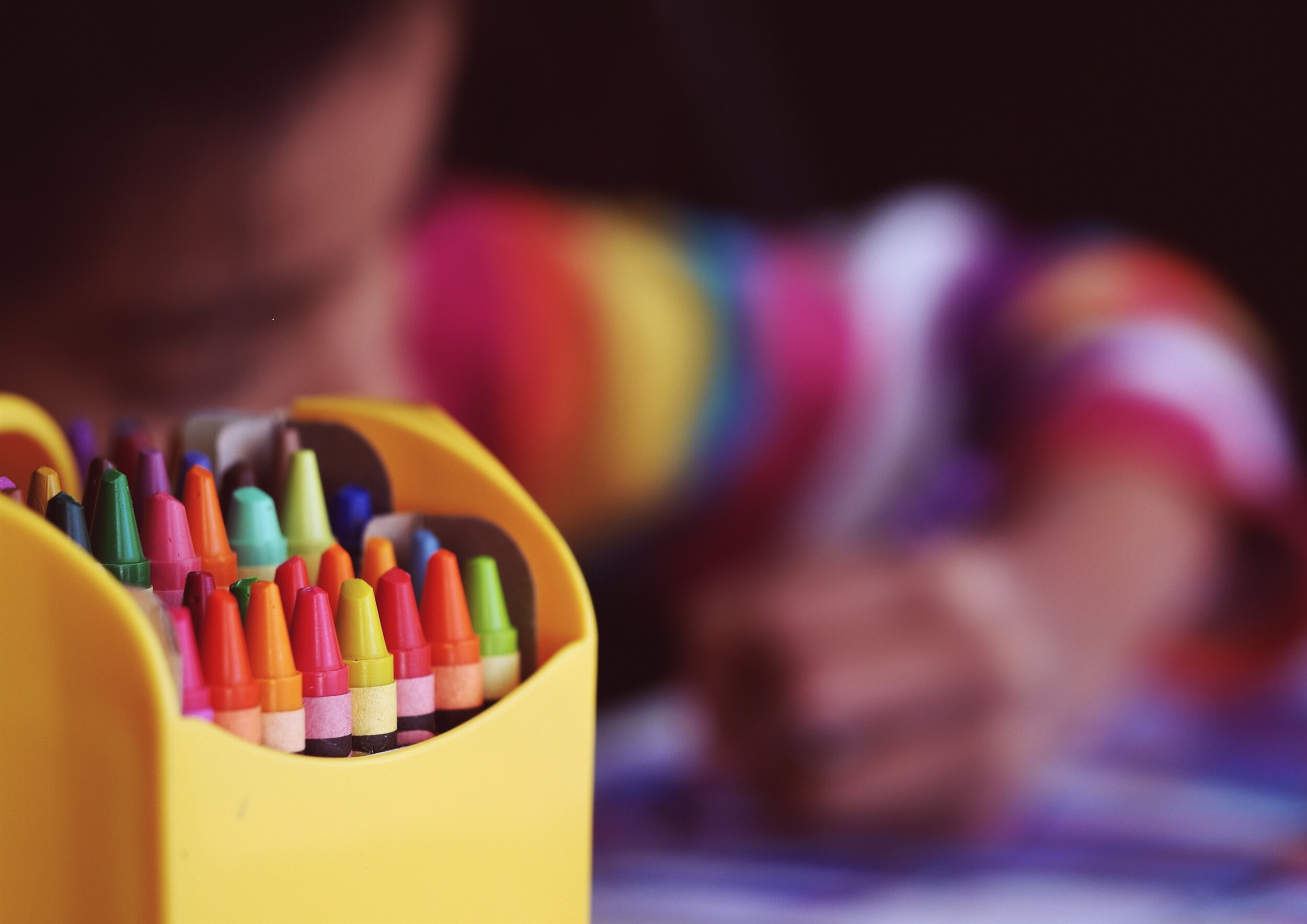 Closeup of a box of Crayons and blurred child colouring in the background