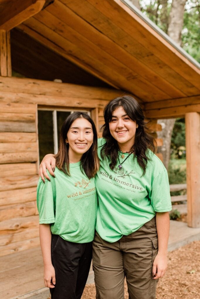 two forest school group leaders posing for a photo outside the wild and immersive research forest headquarters in maple ridge.