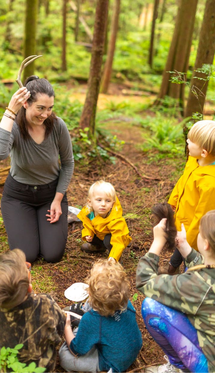 A group of kids listening to a Wild & Immersive program leader who is showing them an antler in the woods