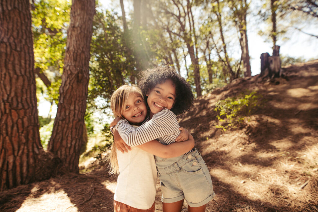 Two girls hugging each other outdoors. Kids together in forest having a great time.