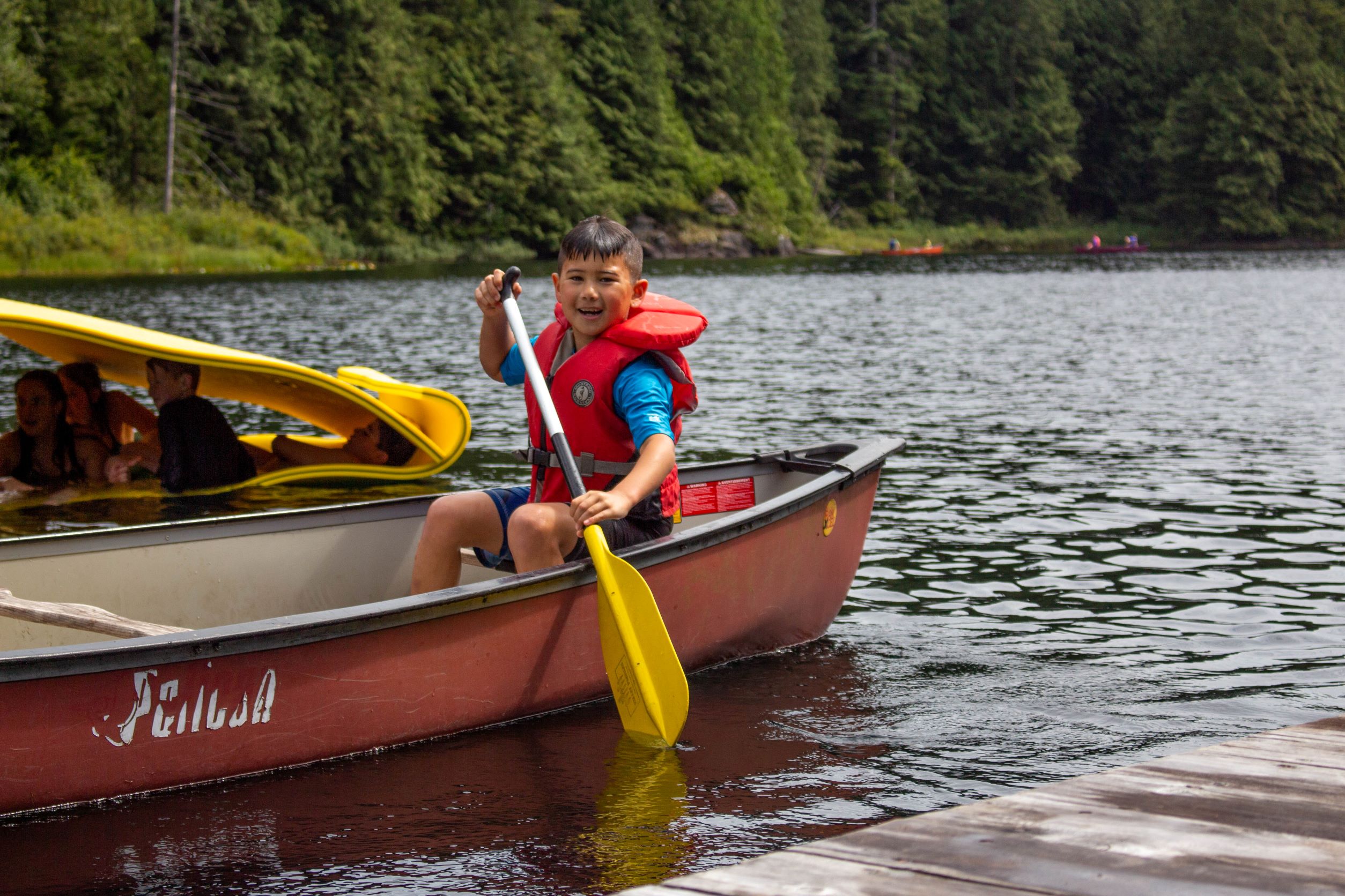 young boy paddling a canoe towards a dock at loon lake during a summer camp