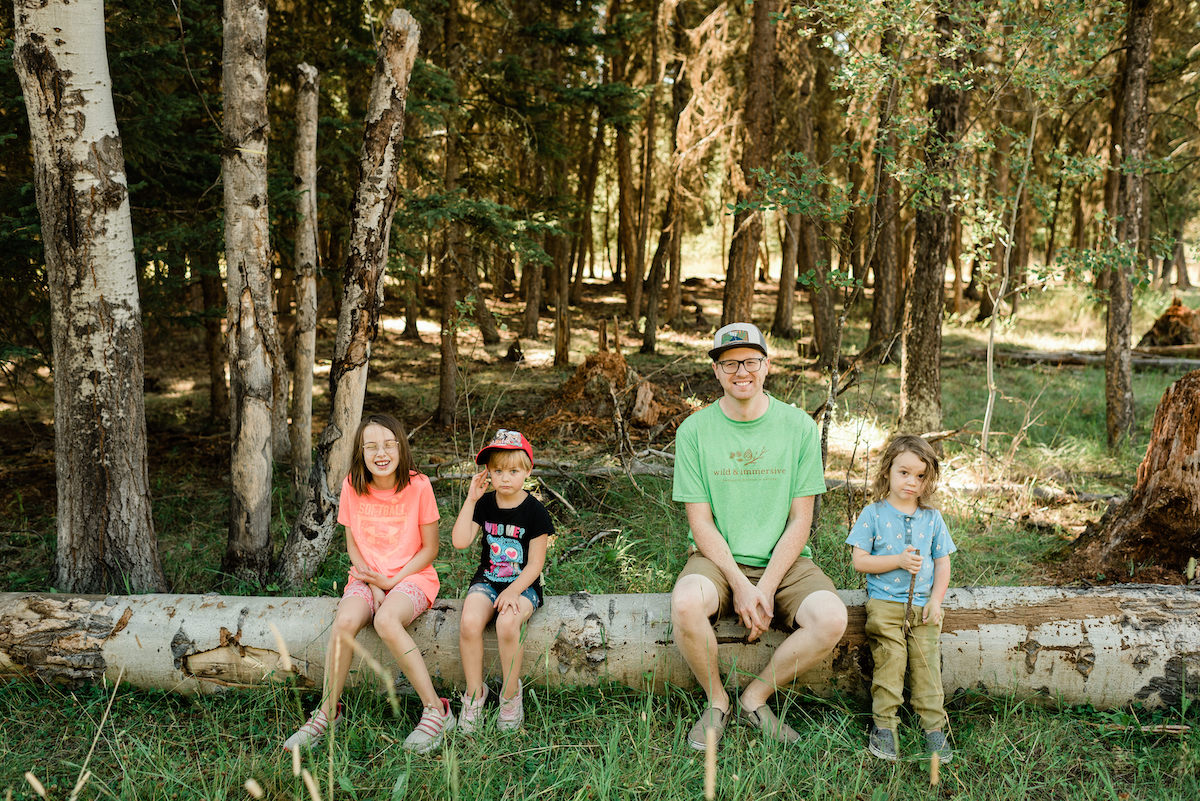 Kids and leader sitting on log smiling at camera at Williams Lake Forest Camp