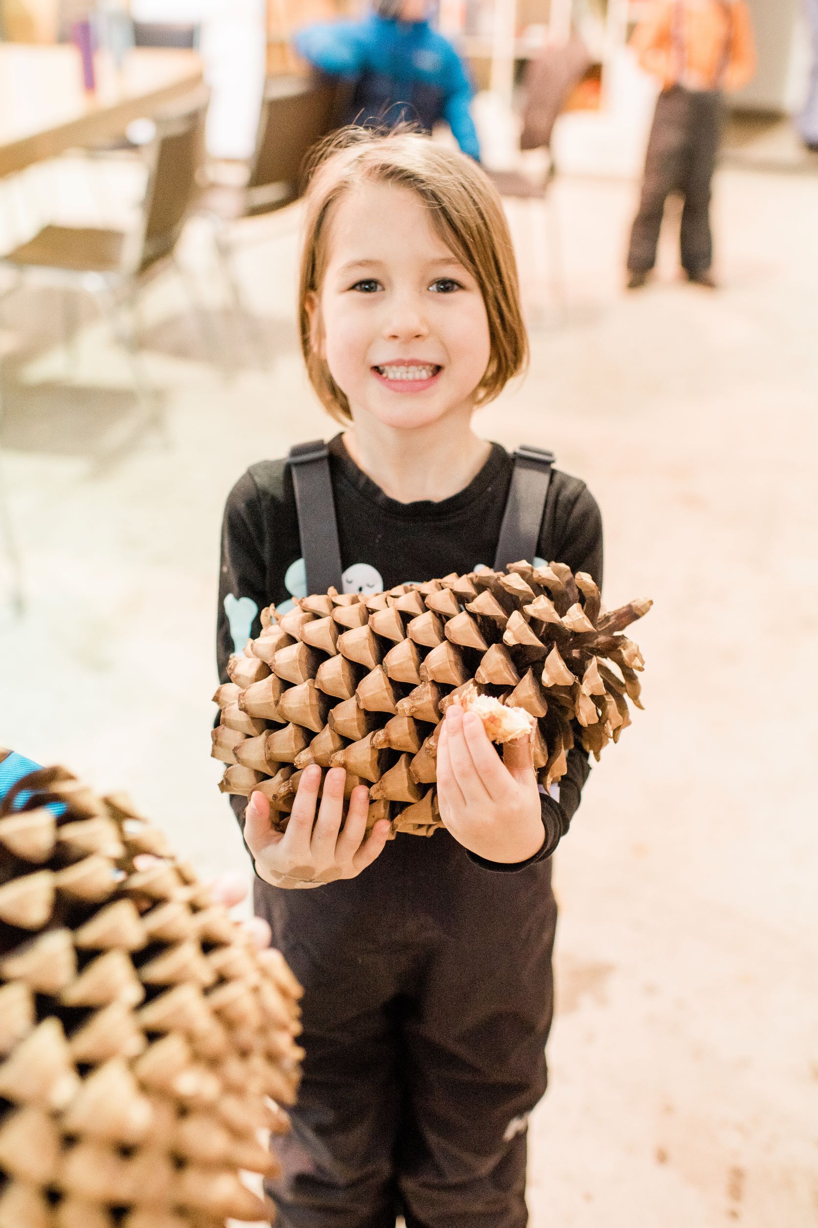 a young girl holding a gigantic pinecone in her arms in a wild and immersive classroom
