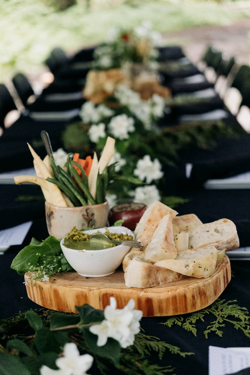 the table spread at the foraging dinner, with black table cloth and tree trunk slices as a platter and vegetables and bread with spread laid out on top