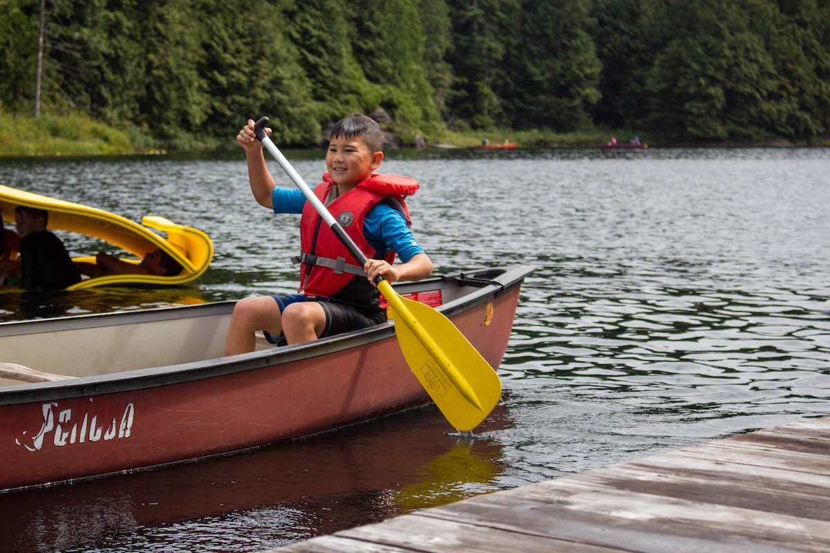 Kid paddling a boat at Loon Lake Wild & Immersive camp