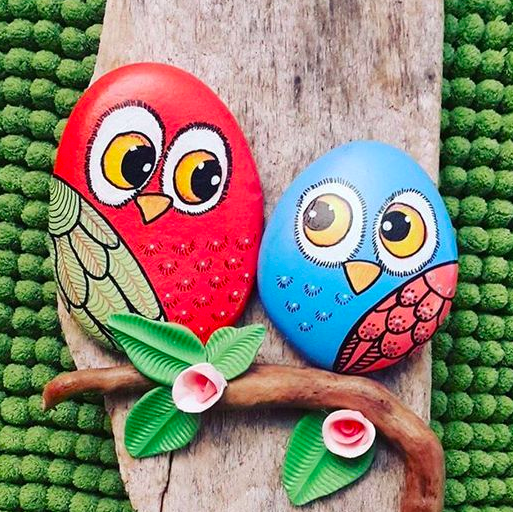 a nature craft of two stones painted to look like owls on a branch, one red and one light blue