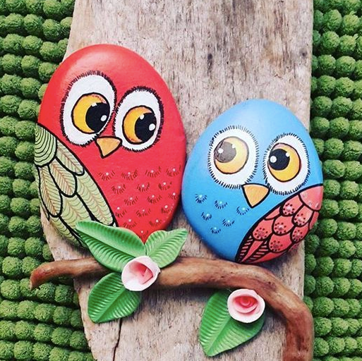 a nature craft of two stones painted to look like owls on a branch, one red and one light blue