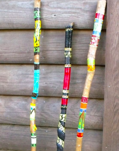 a nature craft of three painted walking sticks with vibrant stripes and patterns, resting on a log barn exterior wall