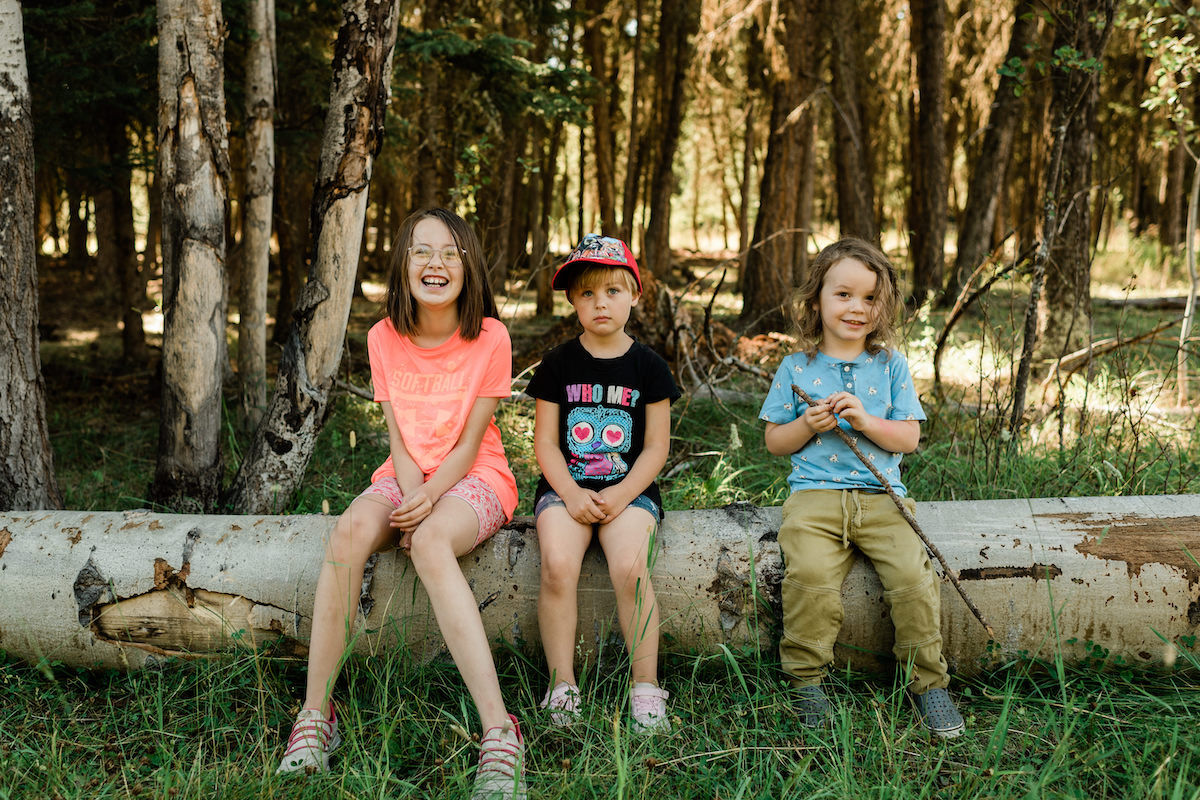 Kids sitting on log smiling at camera at Williams Lake Forest Camp