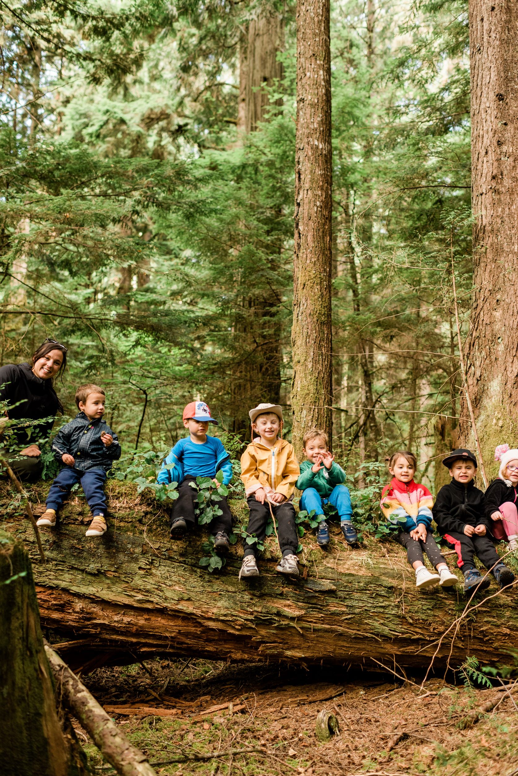 seven young kids sitting on a large log in the forest with a wild and immersive team leader