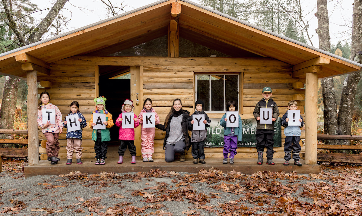 Kids at Wild & Immersive camp in front of a log cabin holding up letters to spell out 